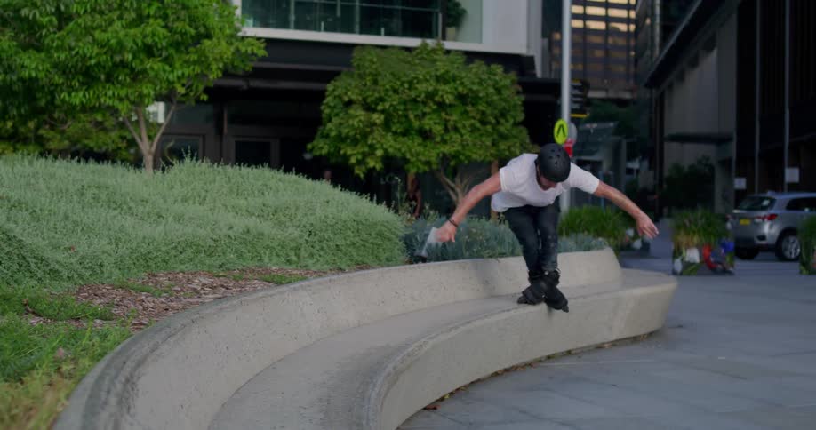A man is rollerblading and performs a trick using a concrete sitting area in a city