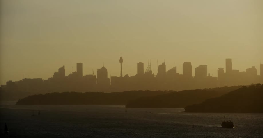 Ship cruises through water away from smog obscured city skyline