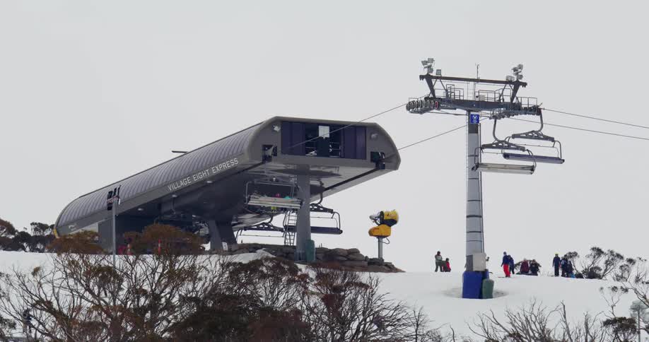 Cable car on the peak of a snowcovered mountain with people around skiing on a cloudy day