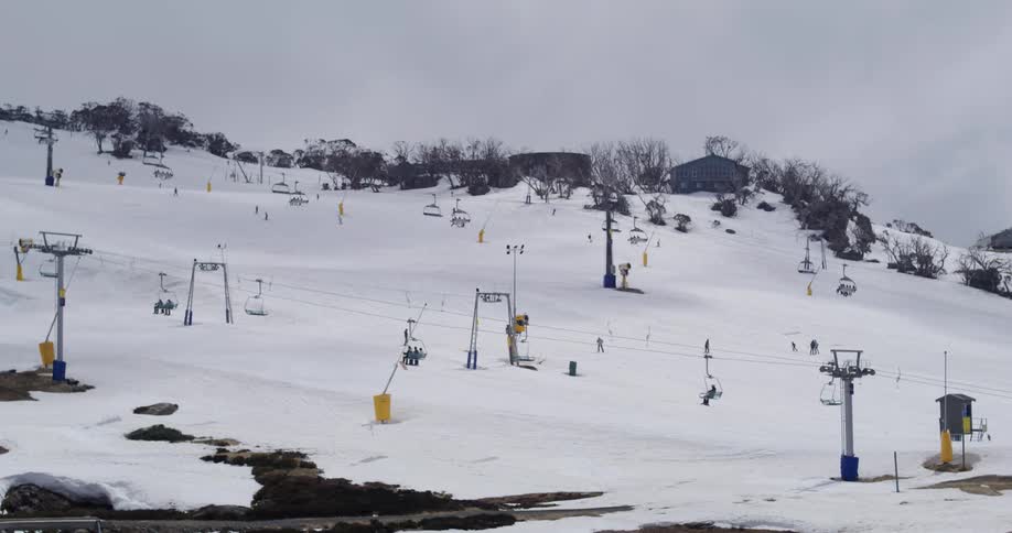 Cable cars amid snowcovered mountains with people skiing on a cloudy day