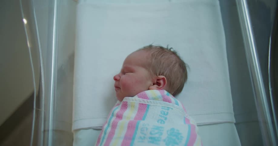 A newborn baby that is swaddled tightly in a blanket rests peacefully