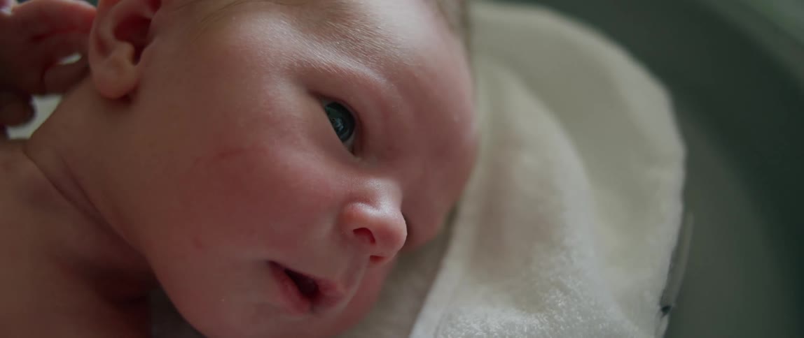 A baby lies on a towel in a crib