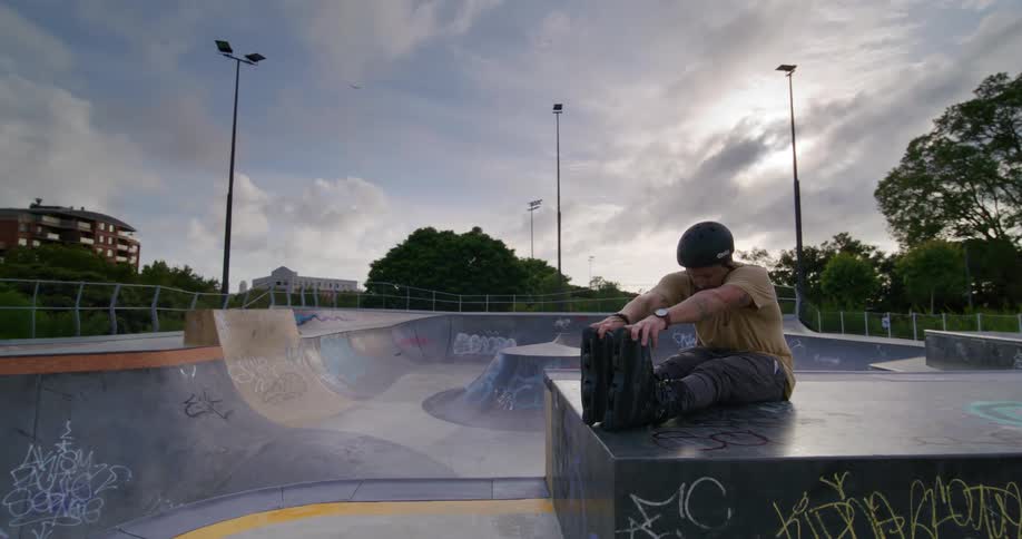 Man stretching his legs while using roller skates sitting at a skate park