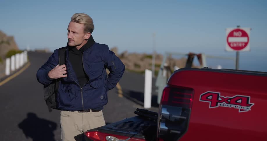 A man picks up a backpack from the trunk of a truck