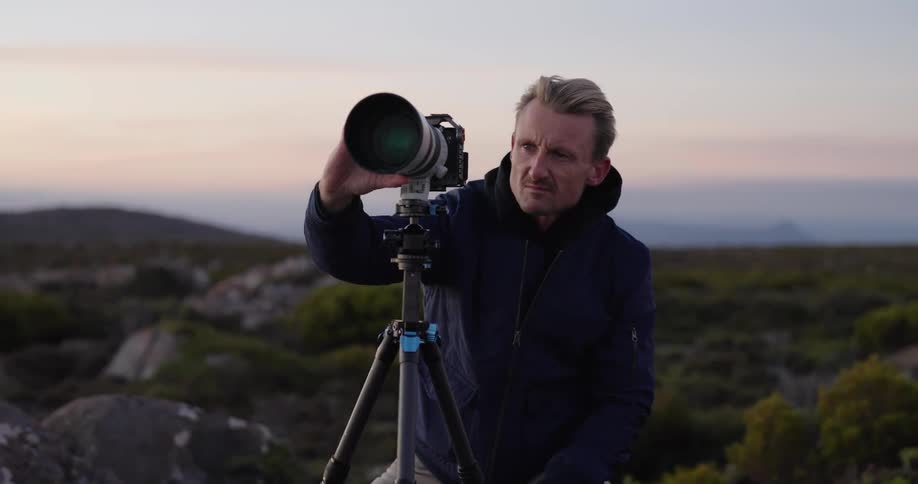 Male nature photographer adjusts the telephoto lens of a camera on a tripod