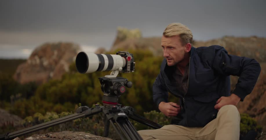 A man outdoors with a camera on a tripod capturing the landscape during dusk