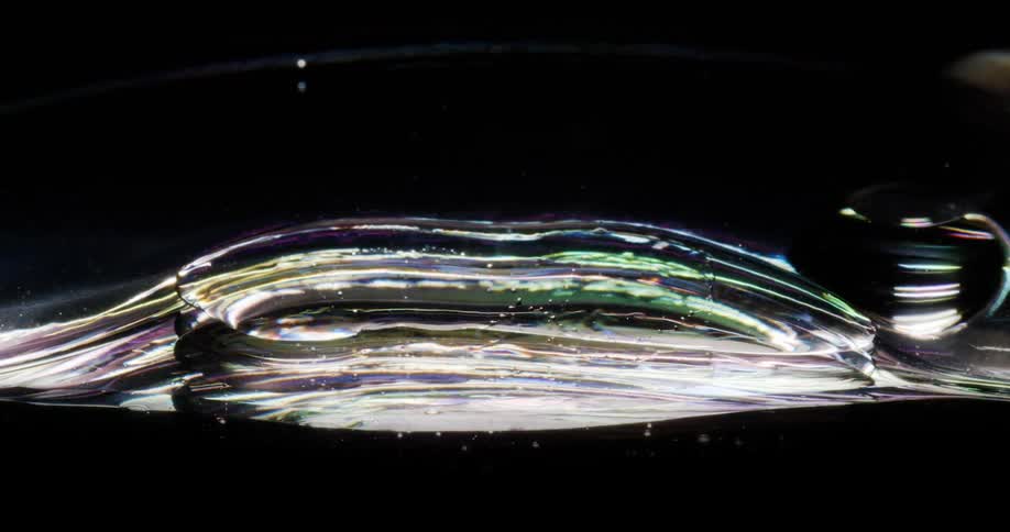 Microscopic view of one bubble coming together into another into a dense shiny liquid