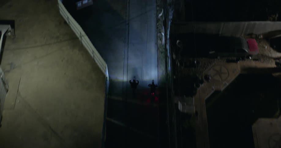 Aerial view of two people riding a motorcycle down a street in a residential neighborhood at night