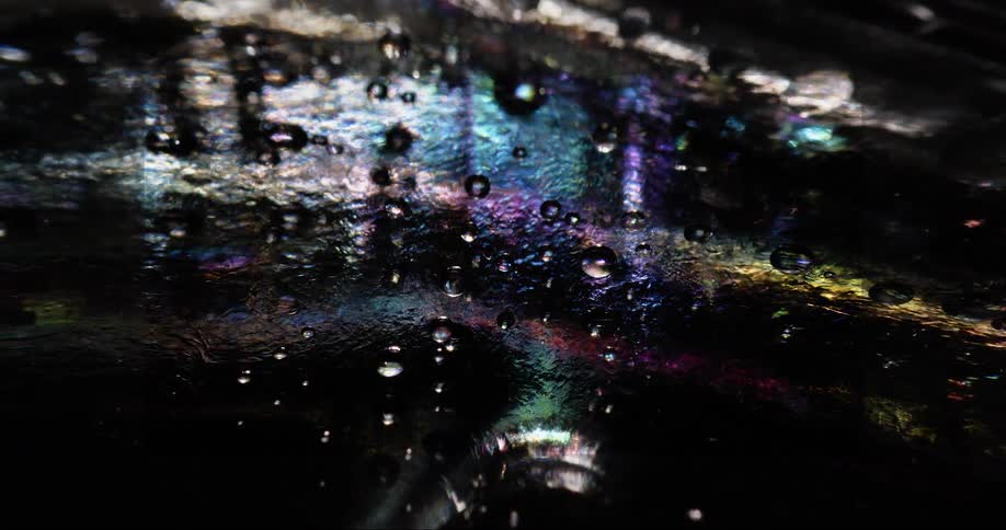 Water beads onclear surface obscuring iridescent mixture at night