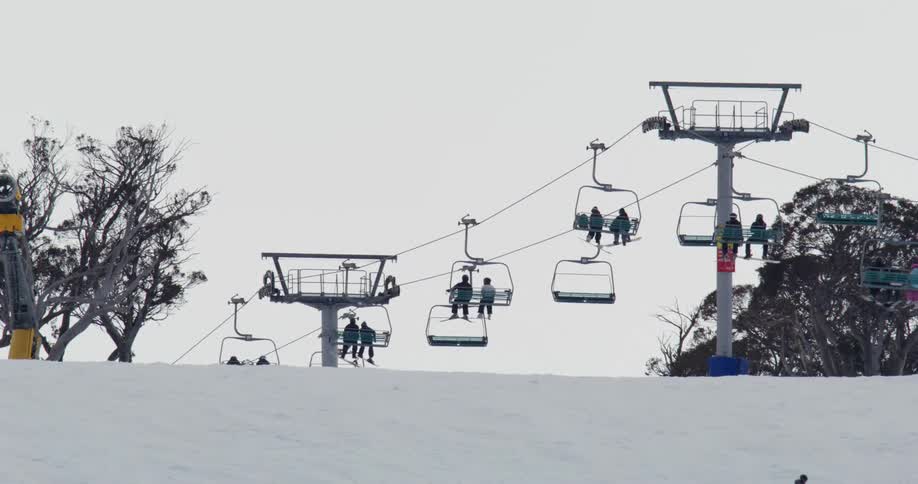 A ski lift transports multiple skiers up a snow covered slope