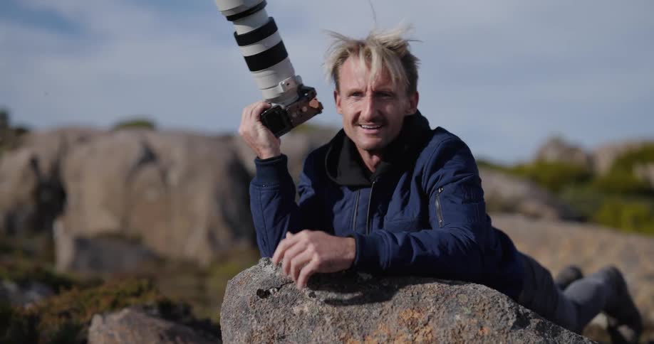 A man reclined on a rock with a camera capturing the landscape