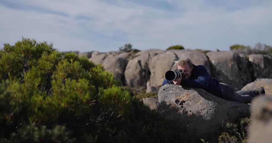 A man lying on a rock photographing the landscape