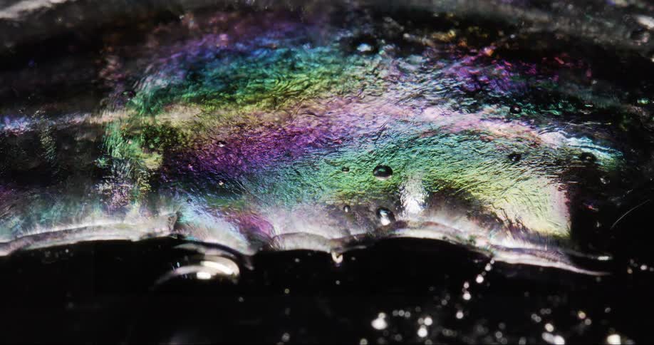 A closeup of a wet oily surface reflecting multicolored lights