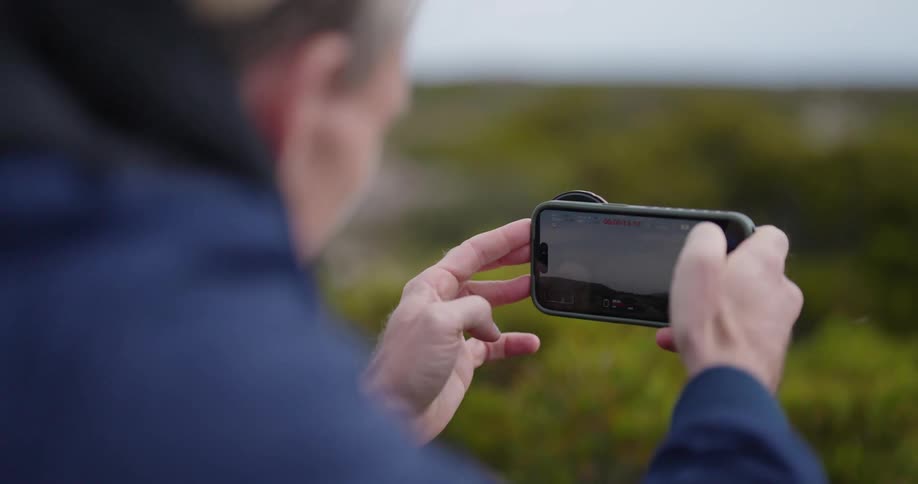 Man with cell phone taking footage outdoors during the day