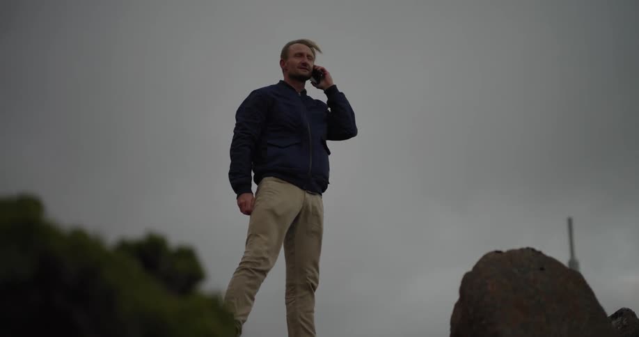 Man standing outdoors on a windy day smiles while talking on smartphone