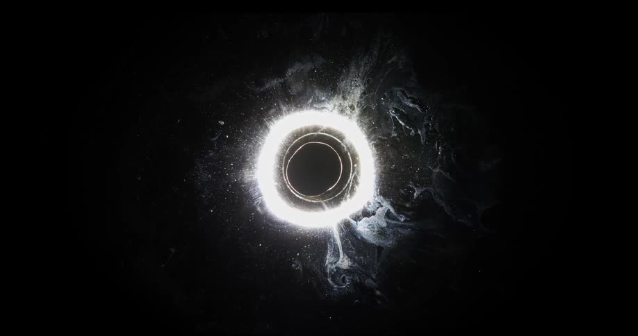 A dark circle in outer space is surrounded by a ring of light
