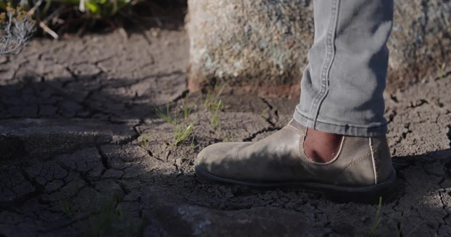 A person wearing boots walks over cracked dirt leaving a footprint