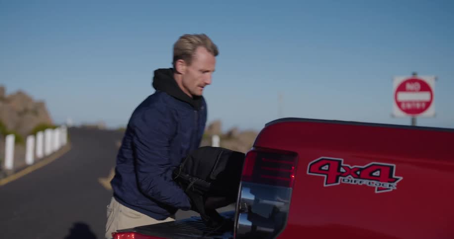 Man opening the trunk of his pickup truck picking up a backpack and a camera tripod