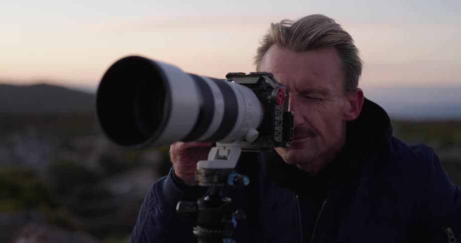 Man looking into the lens of his professional camera with the zoom while standing in a natural environment on a morning