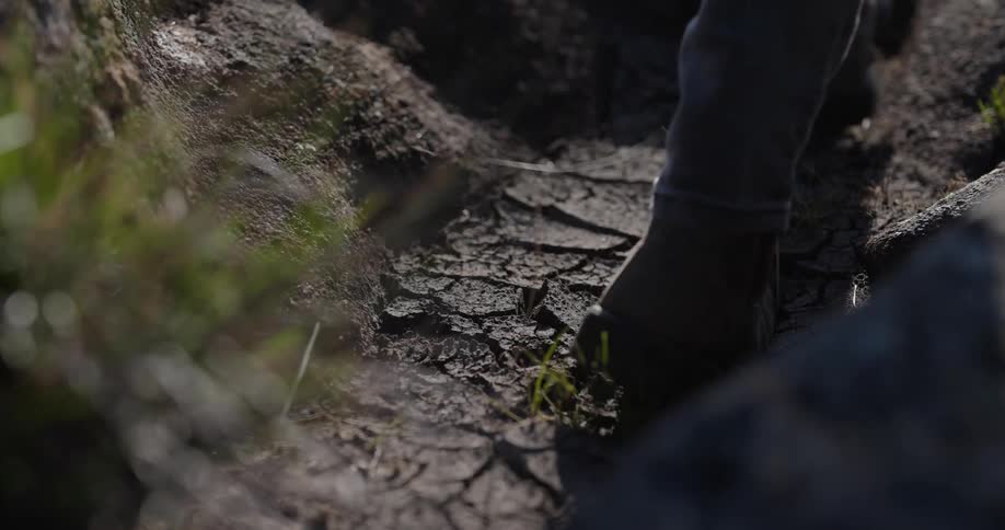 A person with brown boots stepping on the dirt floor