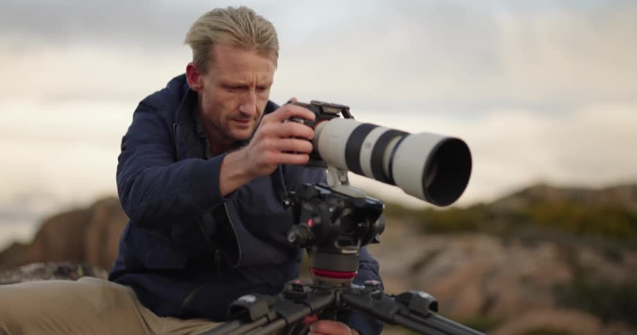 Man adjusting his camera says a professional in a natural outdoor setting with the wind
