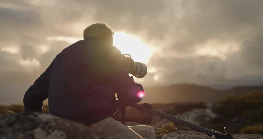 A person is capturing the scenic view of a cloudy sky over the mountains at sunset