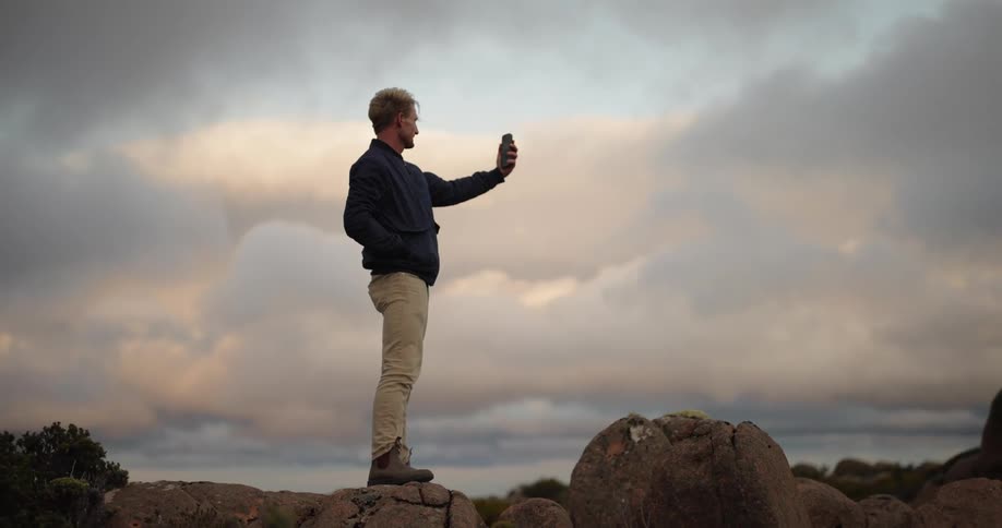 A man trying to signal his cell phone in a desert landscape at sunset