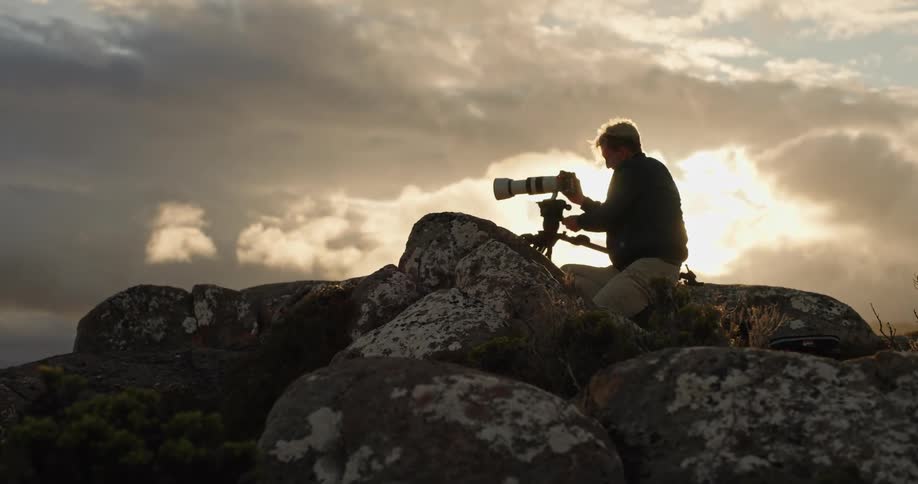 A photographer atop boulders aligns his camera as the sun is low in the sky