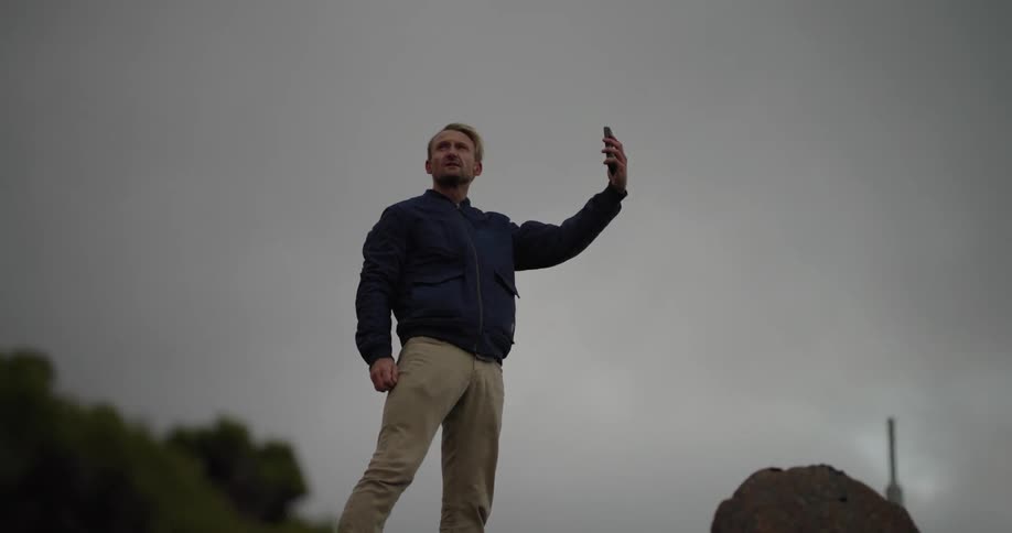 A man stands outdoors in the wind looking at his smartphone