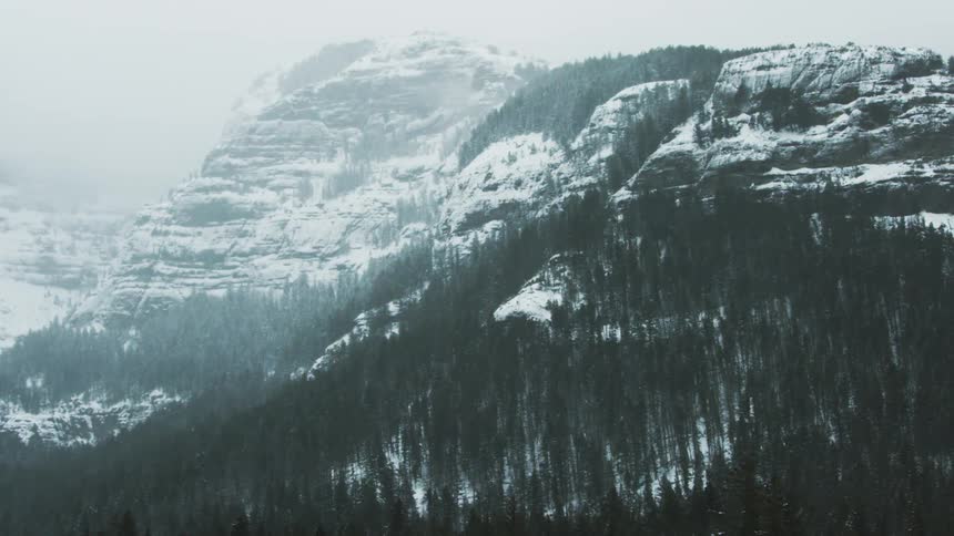 Aerial of a wooded mountain during a winter blizzard