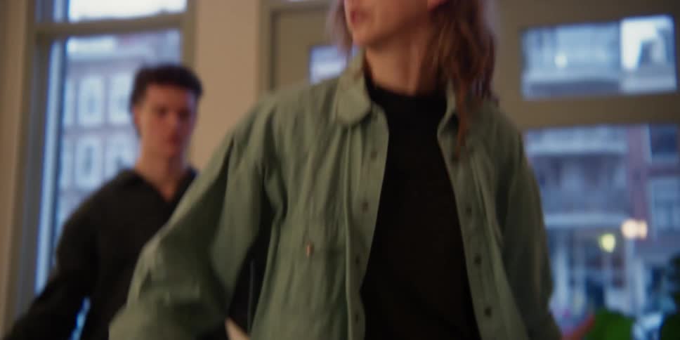 A red-headed Caucasian woman giving dance instruction to a young adult male in a city apartment studio.