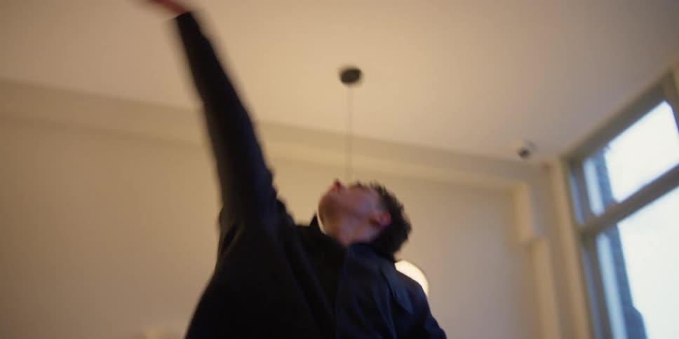 A young adult male dancer practices choreography for a contemporary dance in an apartment studio in the city.
