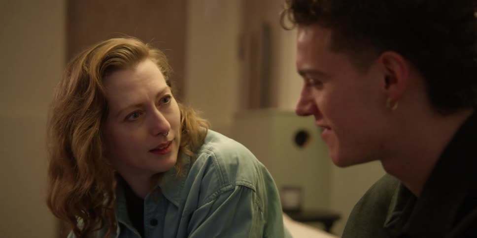 A young man and adult woman are sitting on a couch expressively discussing something they are looking at on a laptop screen and the woman widens her eyes and claps gleefully