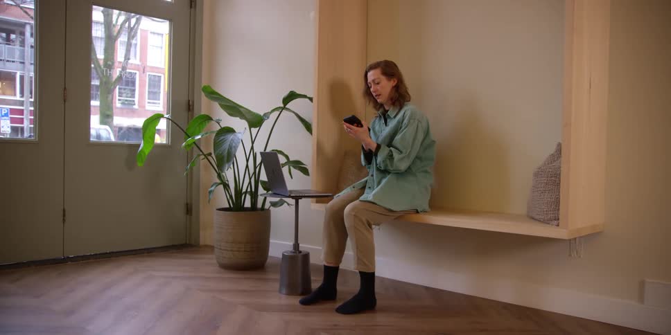 A middle-aged woman puts down her laptop and smartphone before sitting on an apartment floor in a yoga pose.