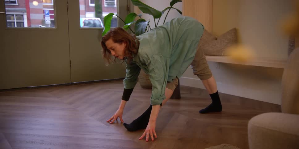 A red-headed woman is stretching and exercising in a city dance studio with windows to the city outside