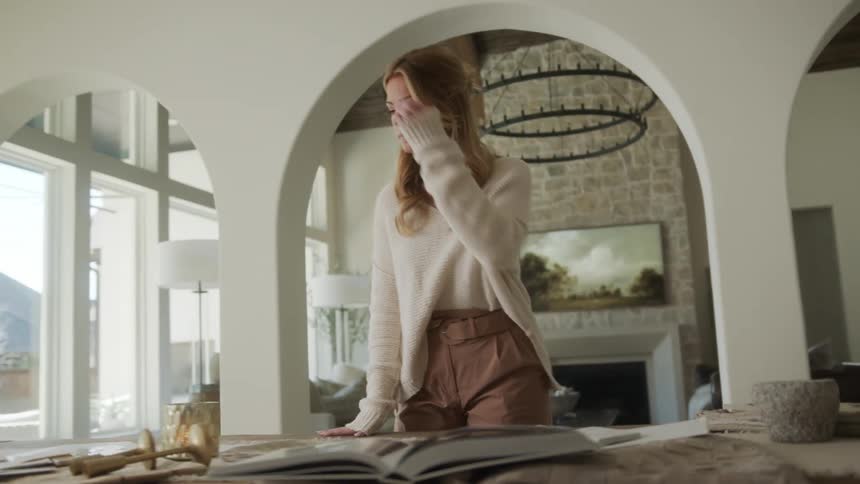 Blonde woman in the living room in front of a table with books and cloths