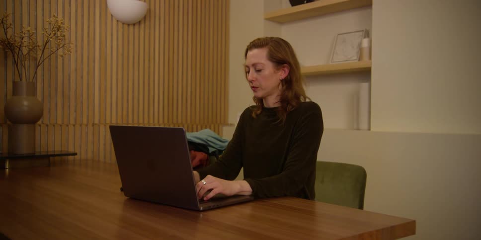 A fair-skinned woman with red hair ends a call on her cell phone as she focuses on her work at her desk in a mid-century modern office.