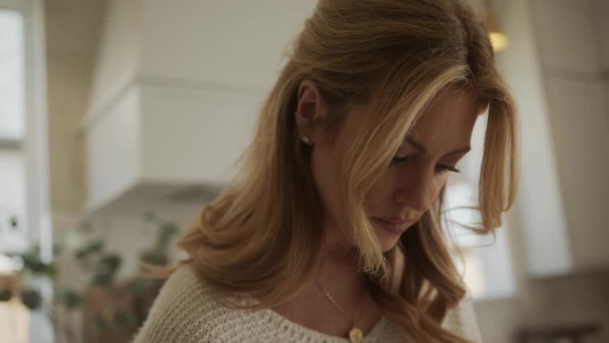 A blonde woman is looking down while focusing intently indoors