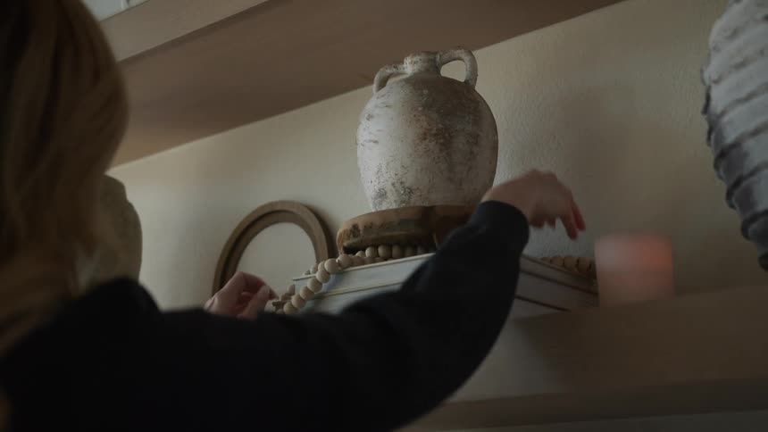 Woman arranging a ceramic vase on top of books on a shelf
