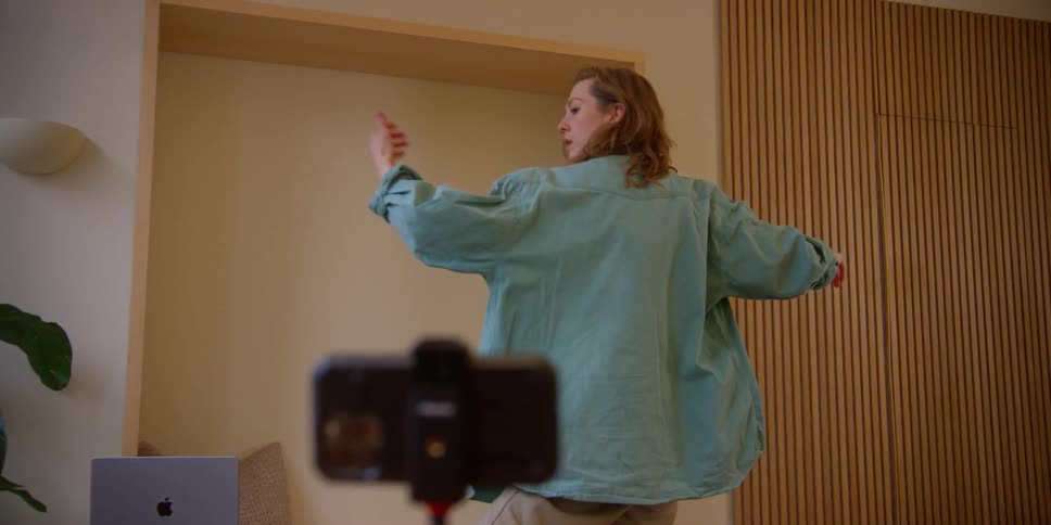 A female dancer practicing contemporary dance choreography while filming herself with a phone camera on a tripod.