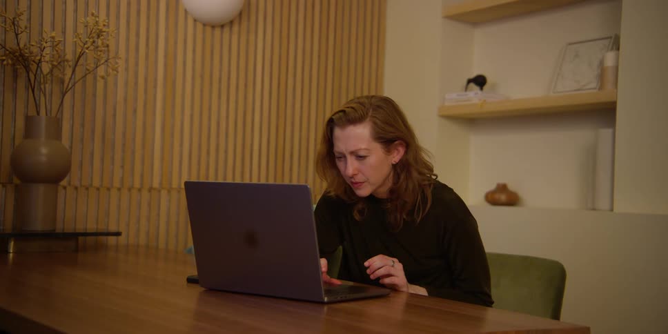 A fair-skinned woman with red hair is viewing dance choreography on her laptop and mirroring the moves with her hands, head, and body.