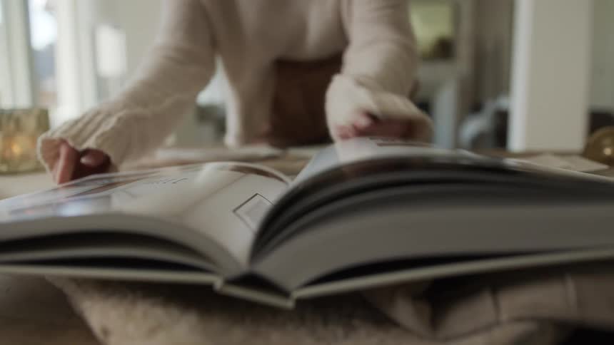 Hands of a woman on a table passing the pages of a book with ceramics around