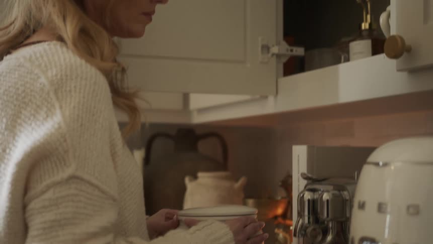 A woman takes down a coffee container from a kitchen cupboard