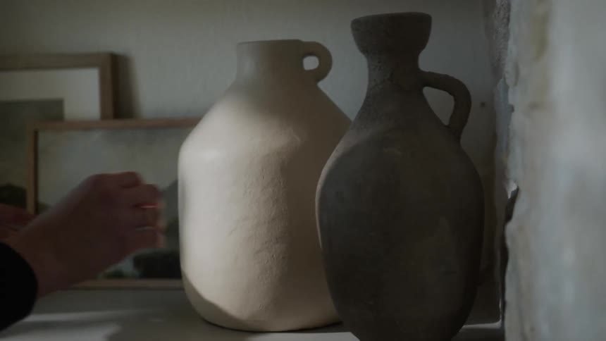 A woman adjusts jugs and photos in her home