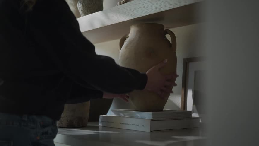Hands of a woman arranging decorative and flower vases on a shelf