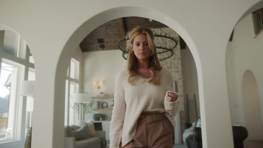 A blonde woman in white clothes is arranging an object on a table placing them from one place to another