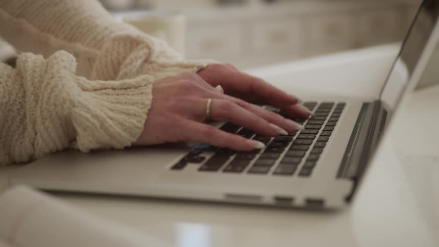 A womans hands typing on a laptop on a white ceramic countertop