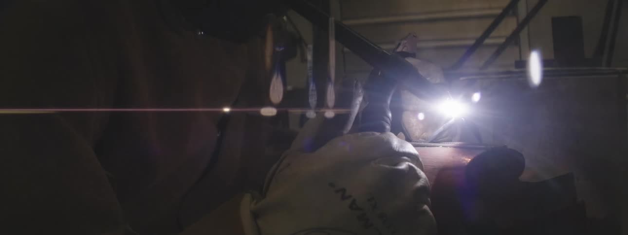 A person is welding with sparks flying in a dimly lit industrial setting