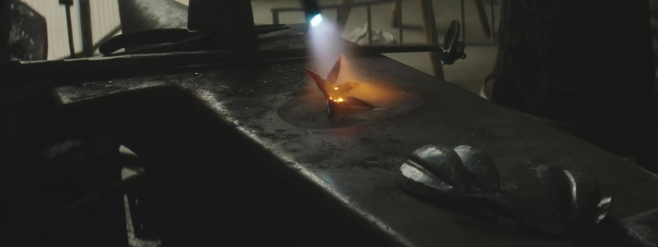 A man is heating metal on the anvil with a torch