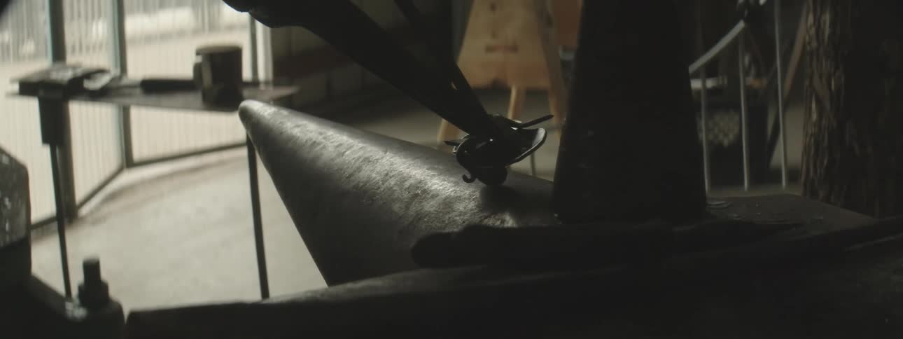 A man using tools to snip and shape metal in a workshop with large windows